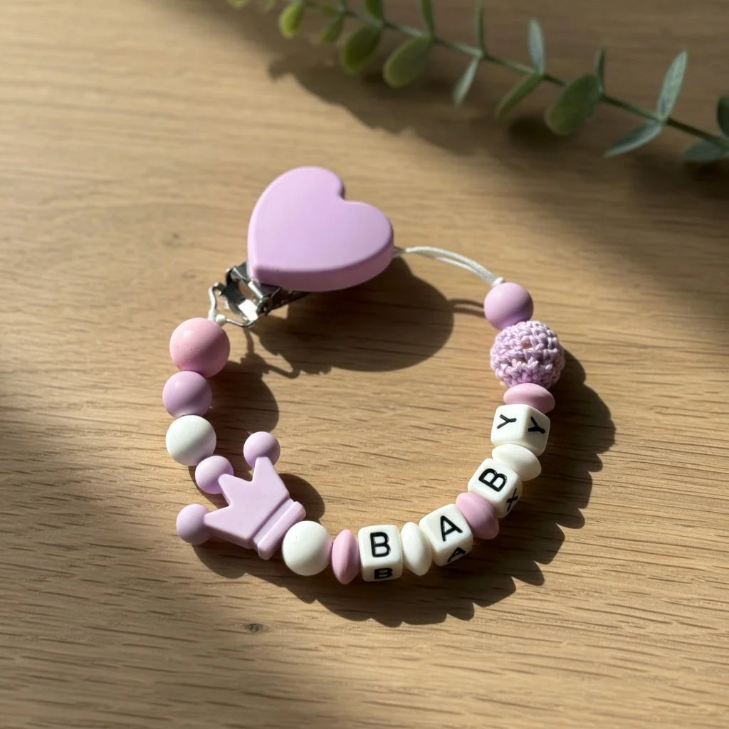 A pink beaded bracelet with a heart charm and custom name beads lying on a wooden surface.