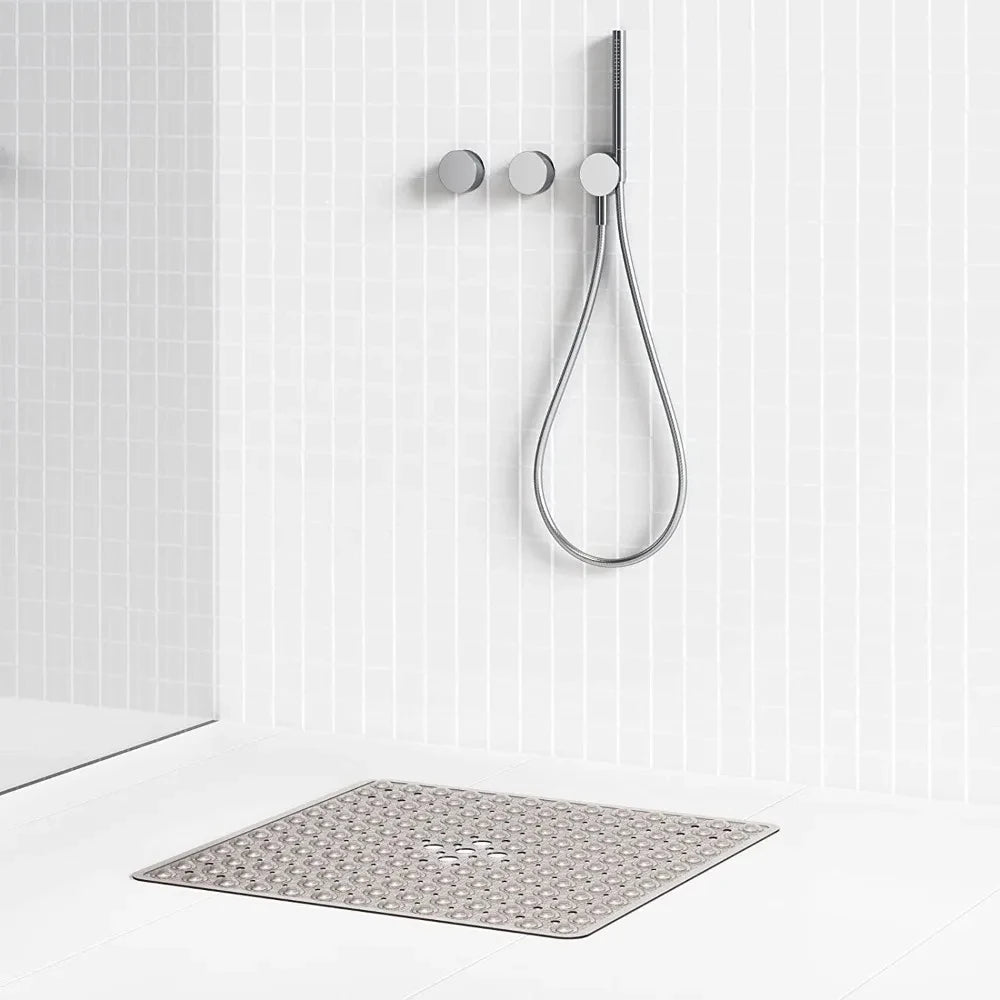 A silver non-slip shower mat with suction cups hangs on a white tiled wall above a bathroom floor.