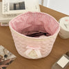 Cesta de acolchado en forma de corazón rosa con forro a cuadros y un lazo de encaje sobre una superficie de madera.