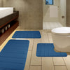 A set of blue plush memory foam bath mats with non-slip backing placed on a tiled floor next to a toilet.