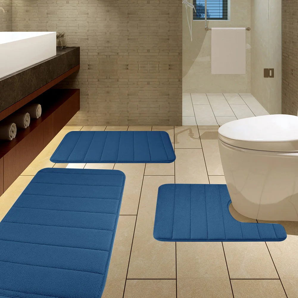 A set of blue plush memory foam bath mats with non-slip backing placed on a tiled floor next to a toilet.