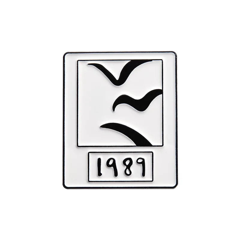 A rectangular enamel brooch featuring a stylized bird silhouette and the year 1989.