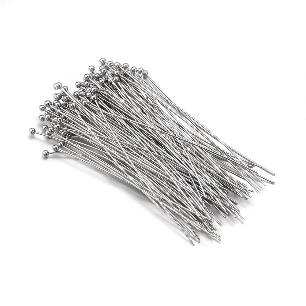 A pile of gold-plated brass ball head pins for jewelry making laid out on a white surface.