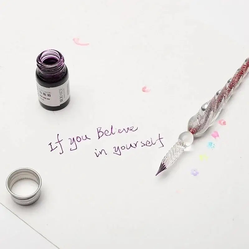 Pluma de inmersión de cristal con tinta dorada junto a texto escrito a mano sobre fondo blanco.
