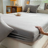 A close-up view of a smooth gray fitted sheet on a bed, with a hand touching the fabric.