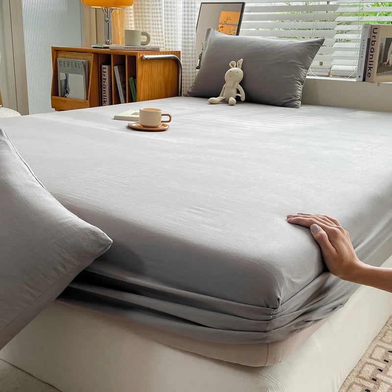 A close-up view of a smooth gray fitted sheet on a bed, with a hand touching the fabric.