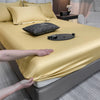 Un lujoso juego de sábanas ajustadas doradas está drapeado sobre una cama, con almohadas y accesorios visibles.