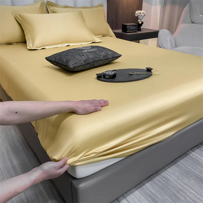 Un lujoso juego de sábanas ajustadas doradas está drapeado sobre una cama, con almohadas y accesorios visibles.