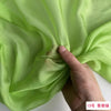 A hand is folding a piece of light green silk chiffon fabric to show its drape and texture.