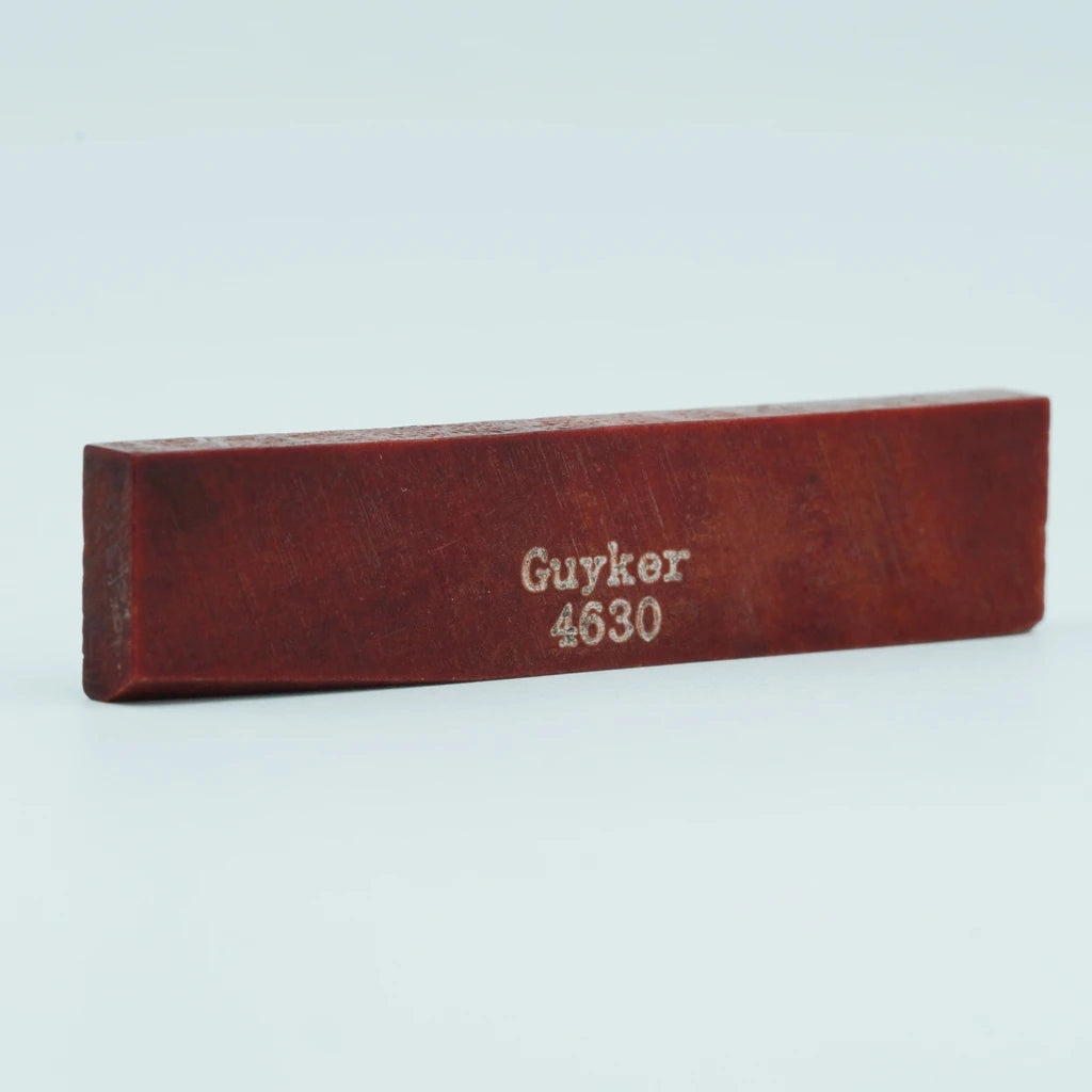A wooden acoustic guitar bridge saddle with the inscription Guyker 4630