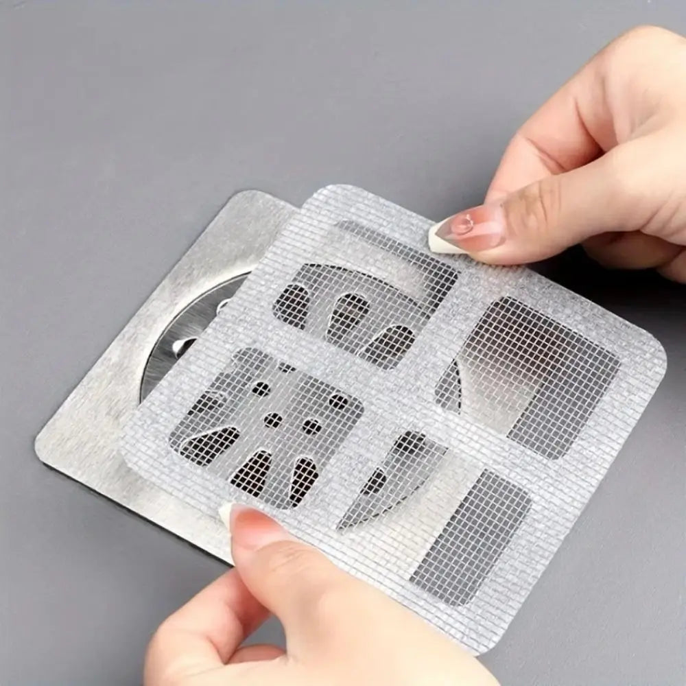 A hand is holding a clear, perforated disposable drain hair catcher sticker on a transparent sheet.