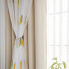 Elegant white and yellow wheat field embroidered curtain with lace trim hanging beside a window.