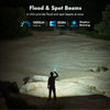 A person is using a flood and spot beam flashlight in an outdoor, rocky environment.