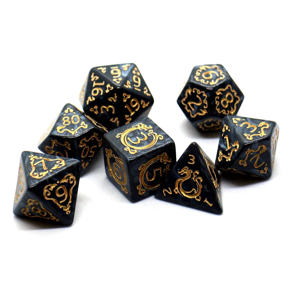A set of black polyhedral dice with gold dragon embellishments scattered on a white surface.