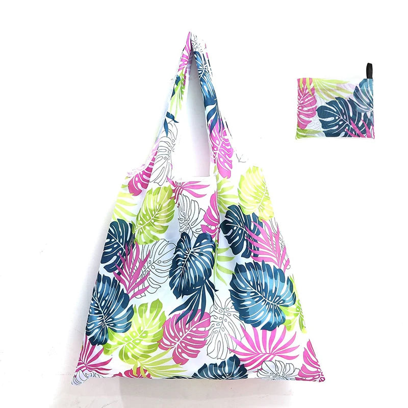 A reusable shopping tote bag featuring a vibrant tropical leaf print in shades of pink, blue, and green.