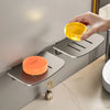 A hand is pouring yellow liquid soap into an aluminum wall-mounted soap dish with a drain.