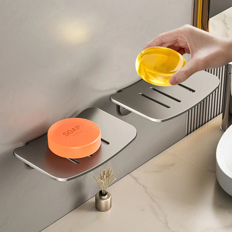 A hand is pouring yellow liquid soap into an aluminum wall-mounted soap dish with a drain.