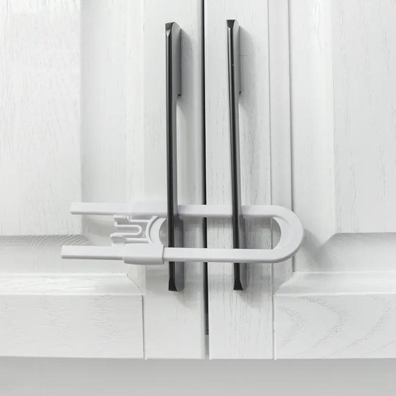 A close-up of adjustable U-shaped cabinet locks installed on a white wooden door frame.