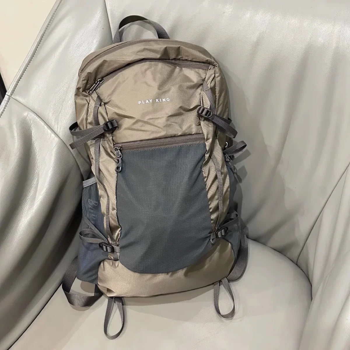 A tan and gray lightweight waterproof travel backpack resting on a light leather couch.