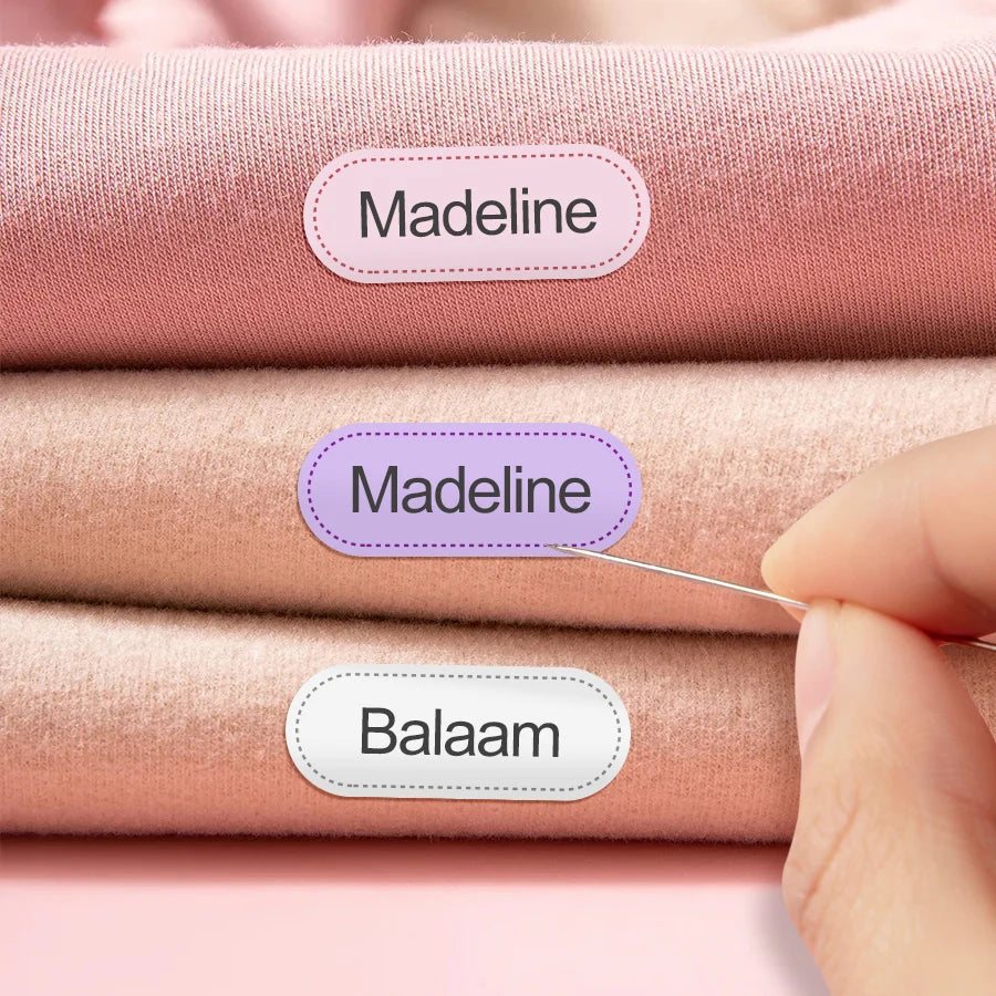 Tres piezas de tela rosa con etiquetas de nombre para ropa, incluyendo Madeline y Balaam.