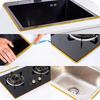 Close-up view of a black cooktop and stainless steel sink with decorative gold trim and self-adhesive tile gap tape.