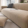 A beige quilted stretch sofa cover with a textured weave and a dark gray throw pillow on a light-colored sofa.