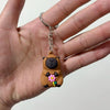 A small, brown capybara charm keychain is being held on a person's finger.