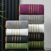 A stack of luxury bath towels in various colors including purple, gray, white, black, and olive green with gold stripes.