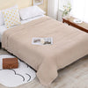 A beige muslin throw blanket is draped over a bed, with white pillows and a small wooden box nearby.