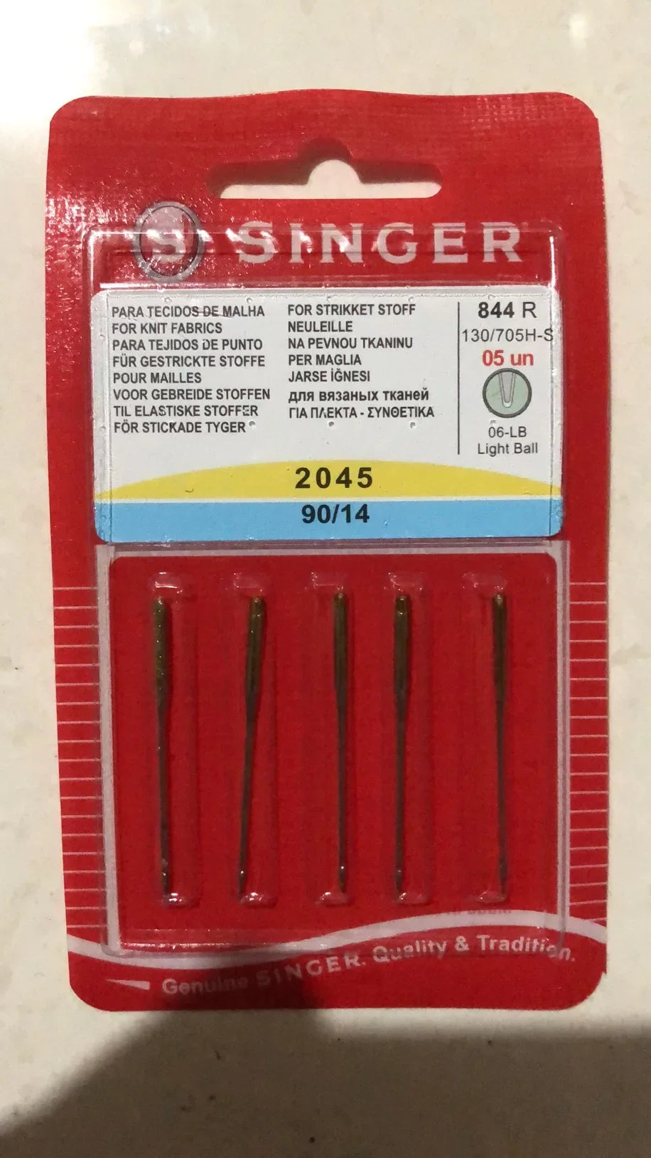 A red plastic package containing a 5-pack of Singer sewing machine needles labeled for various fabrics.