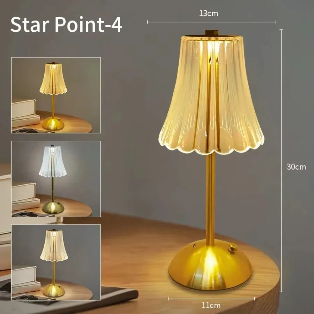 A tall, gold-toned table lamp with a translucent pleated shade is shown on a wooden surface.