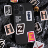 A black smartphone is surrounded by various vintage alphabet stickers, including J, I, H, and Z.