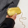 A hand holds a mini gold metal clutch bag against a dark gray fabric background.