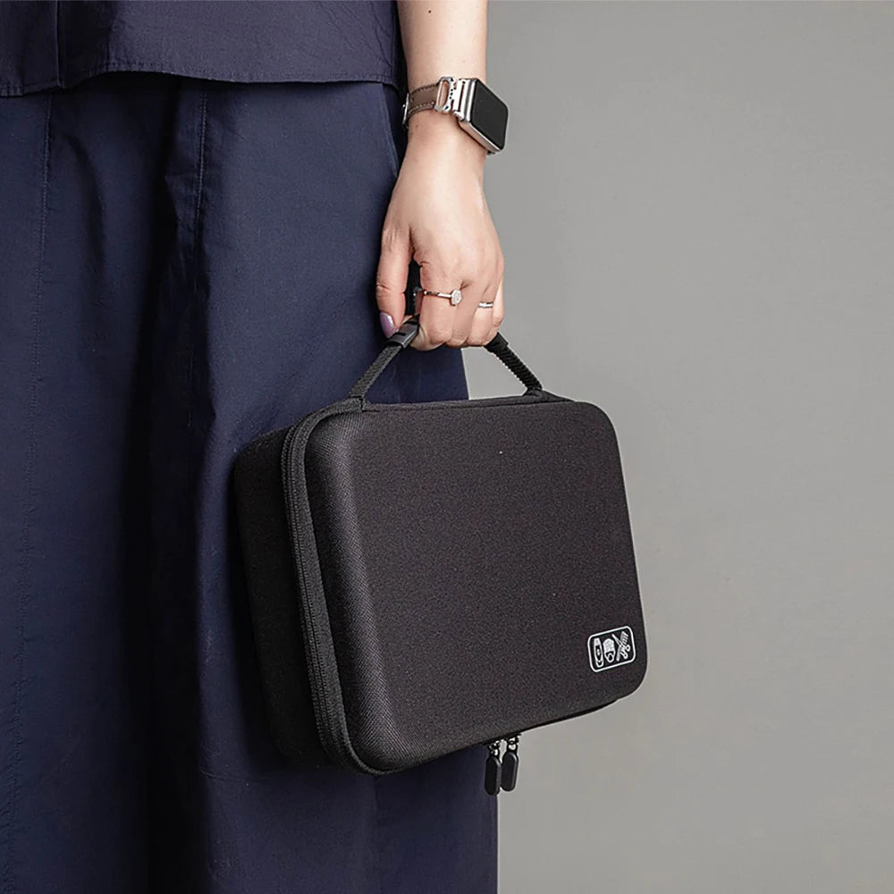 A black hard-shell travel case for hair clippers and accessories is held by a person wearing a dark blue garment.