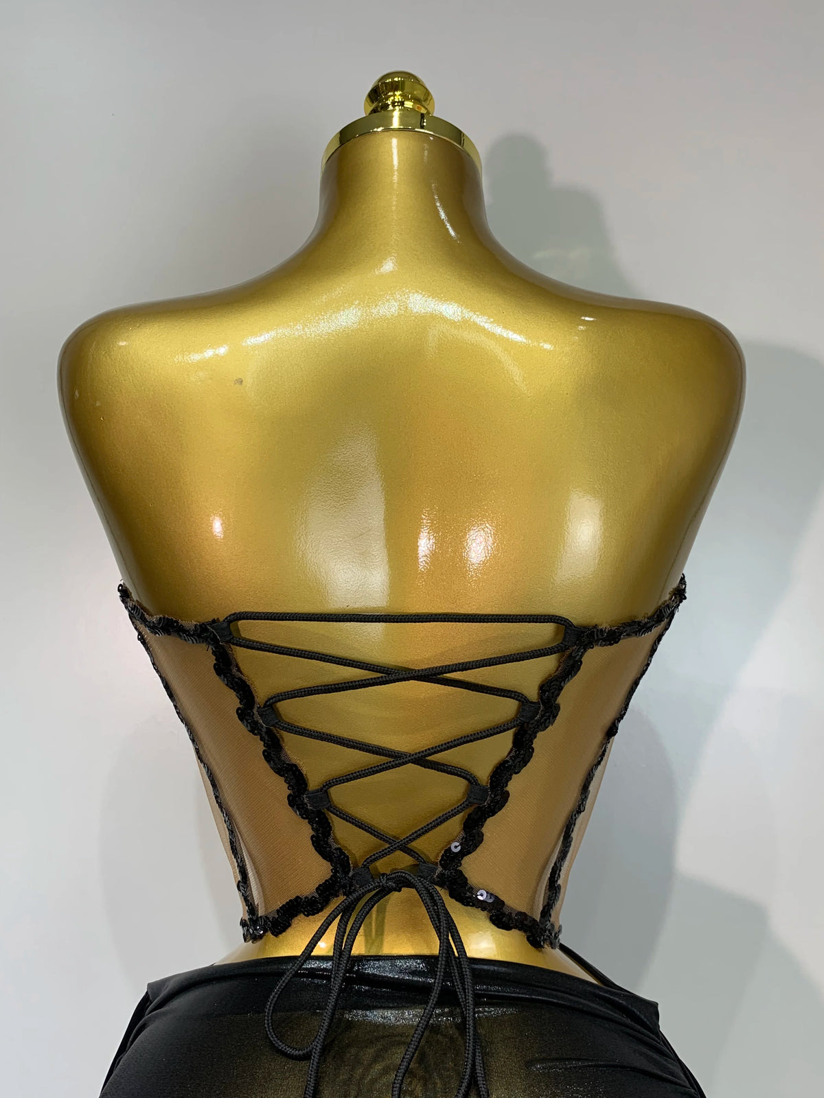 A gold-toned mannequin displays a black, laced two-piece party outfit with a see-through top.