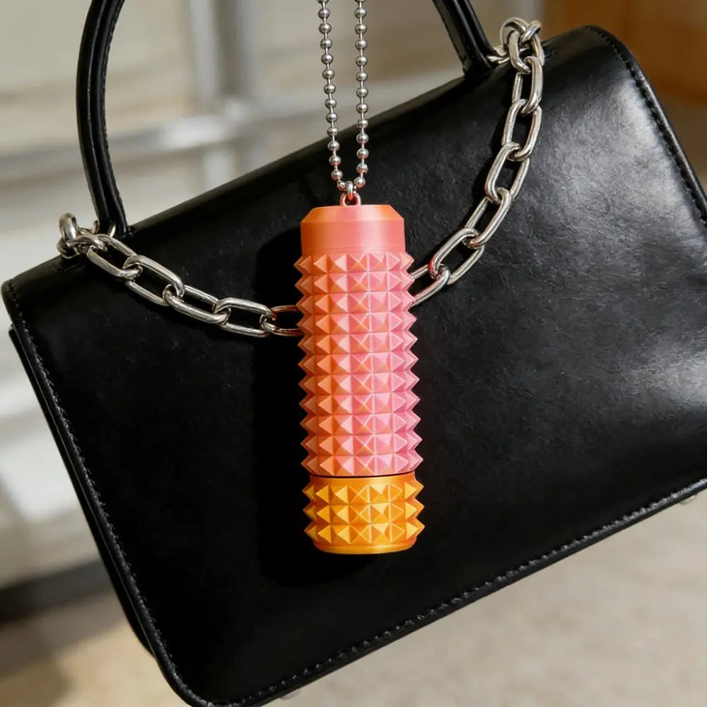 A spiky sensory fidget roller in orange and yellow is hanging from a silver chain against a black handbag.