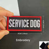 A hand holds an embroidered patch for a service dog with the text SERVICE DOG on a black fabric background.