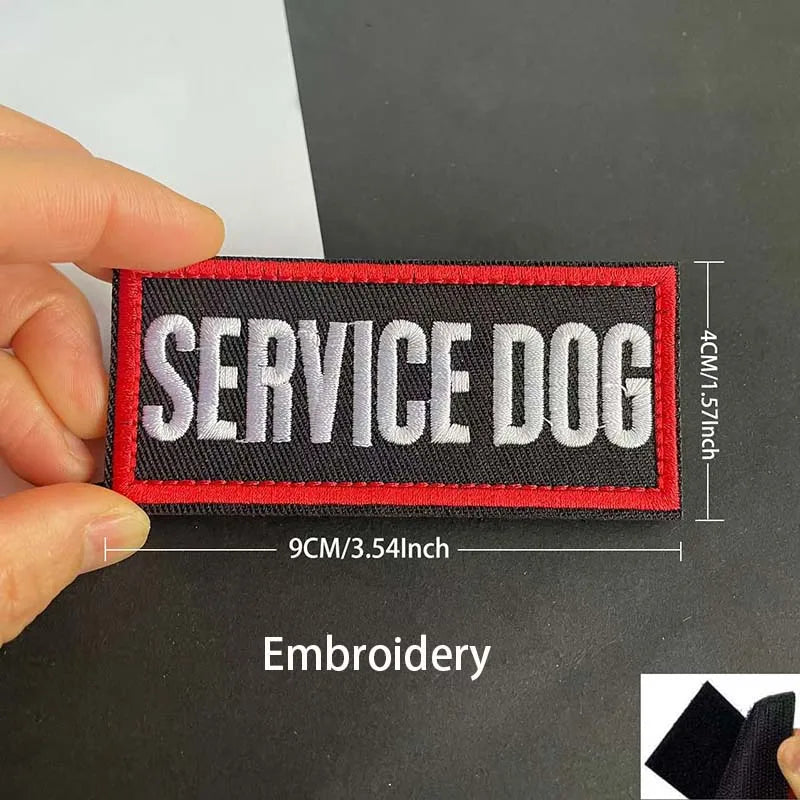 A hand holds an embroidered patch for a service dog with the text SERVICE DOG on a black fabric background.