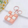 A pink and white tactile clicking keyboard keychain fidget toy resting on a white surface next to a flower.