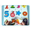 A hand is placing puzzle cards featuring numbers and shapes onto a blue board for a Montessori matching game.