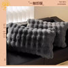 A dark gray, fluffy quilted pillow is shown resting on a black surface.