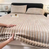 A beige knitted fitted bed sheet with vertical ribbing is spread across a bed, flanked by matching pillows.