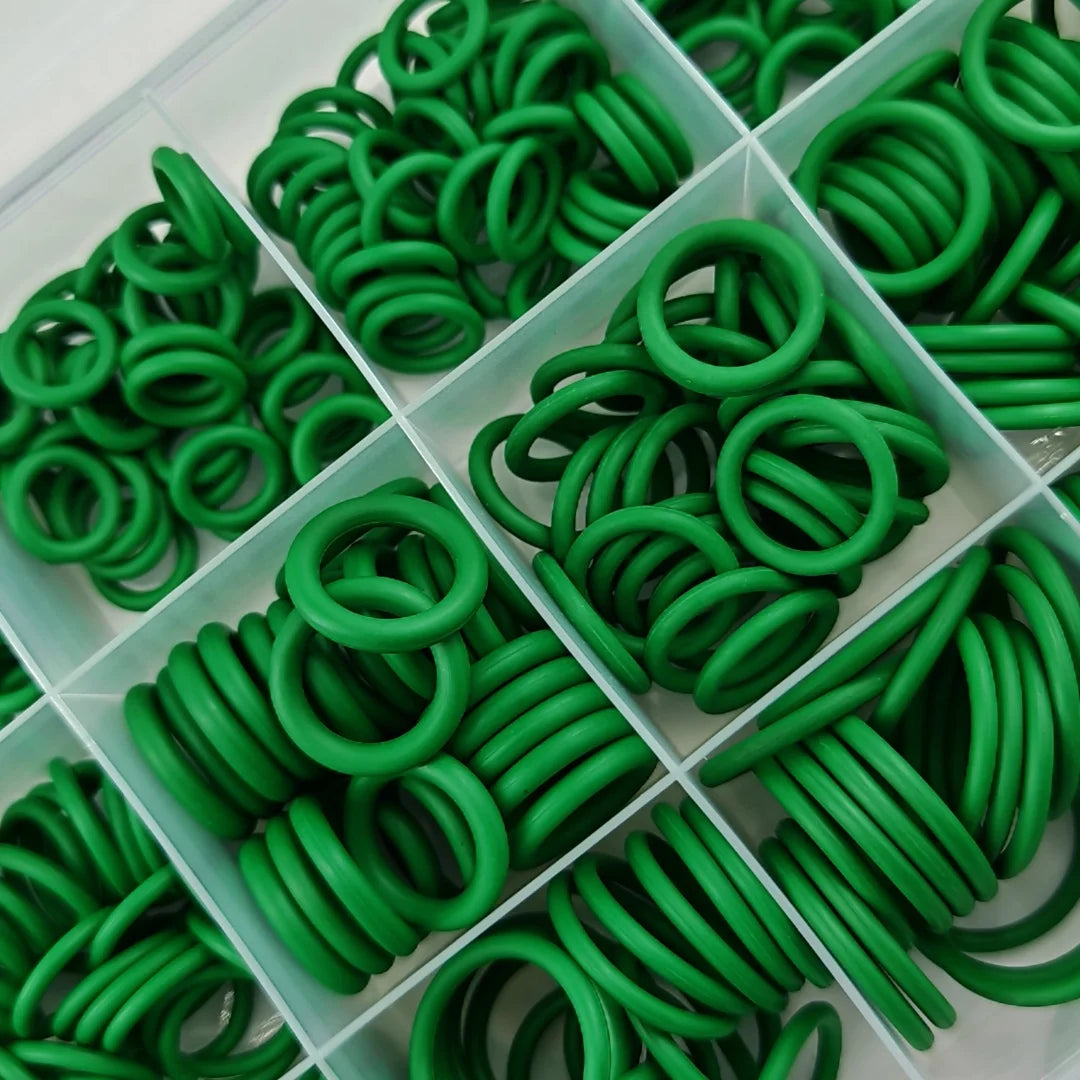A variety of green automotive air conditioning O-ring gaskets are arranged in a clear plastic tray.