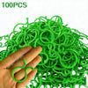 A hand holds a large quantity of 100 green reusable garden plant support clips or vine strapping ties.