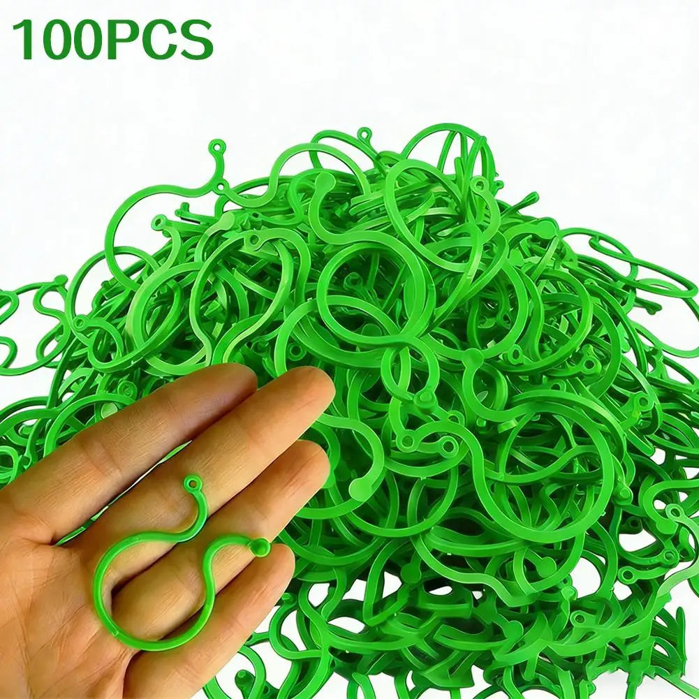 A hand holds a large quantity of 100 green reusable garden plant support clips or vine strapping ties.