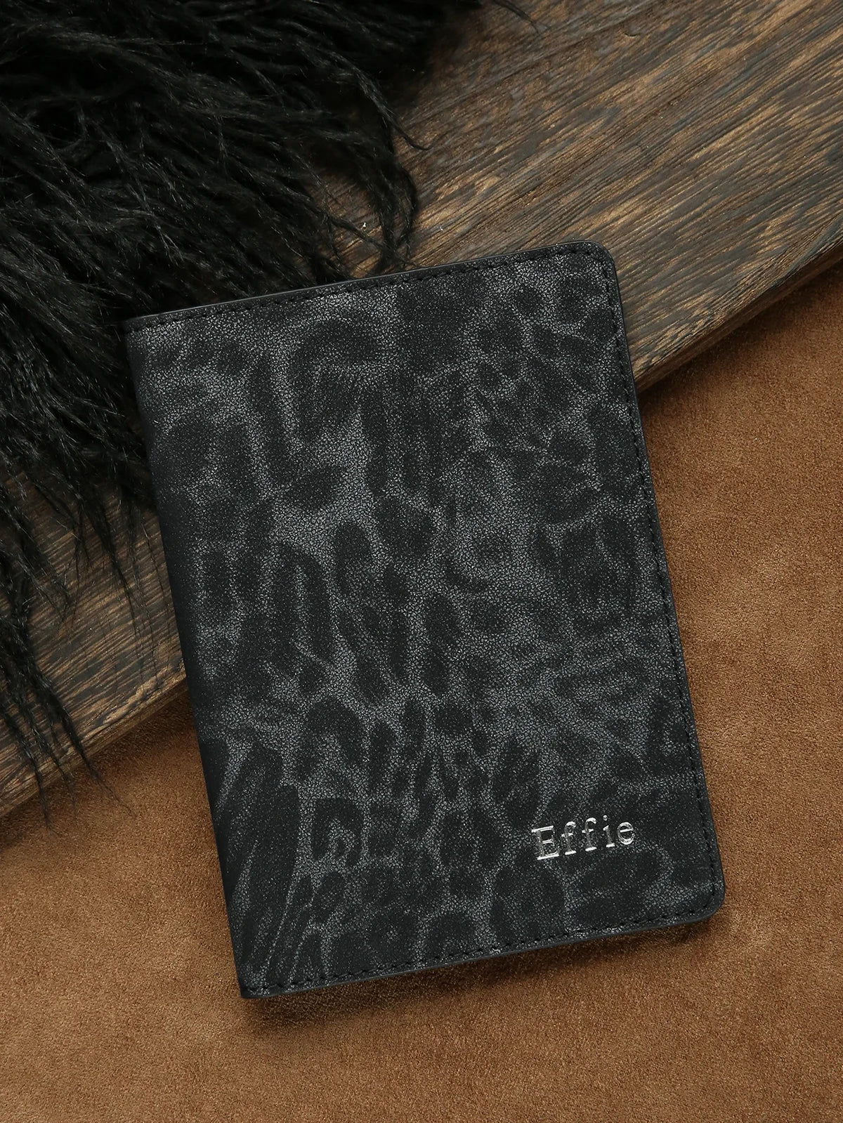 Black leopard print passport holder with personalized name embossing resting on a brown surface.
