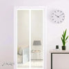 A white framed mirror reflects a room interior, with a black wall clock and a potted plant visible.
