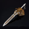 A detailed metal sword keychain featuring a gold-colored blade and hilt, mounted on a rough stone, against a dark background.