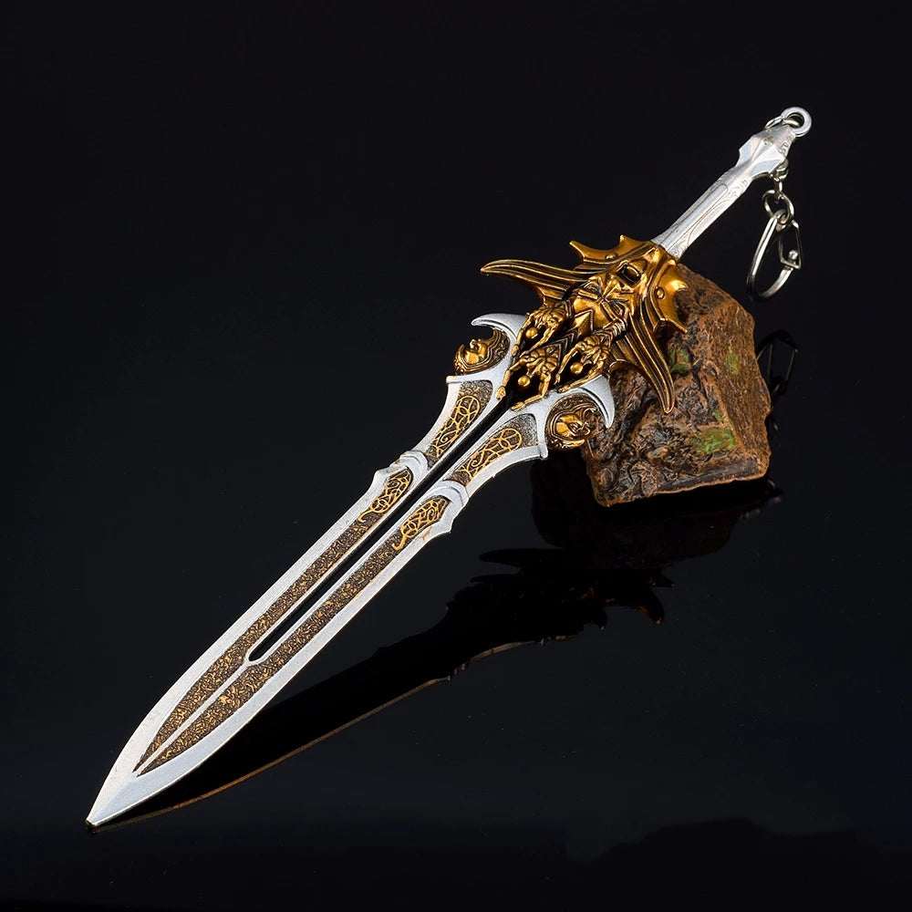 A detailed metal sword keychain featuring a gold-colored blade and hilt, mounted on a rough stone, against a dark background.