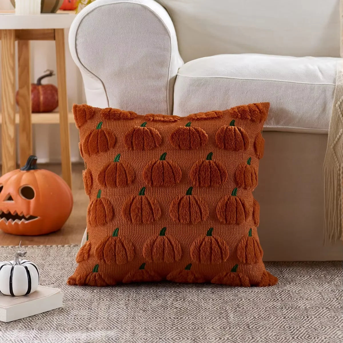 An orange plush throw pillow covered in repeating green pumpkin patterns resting on a gray rug.